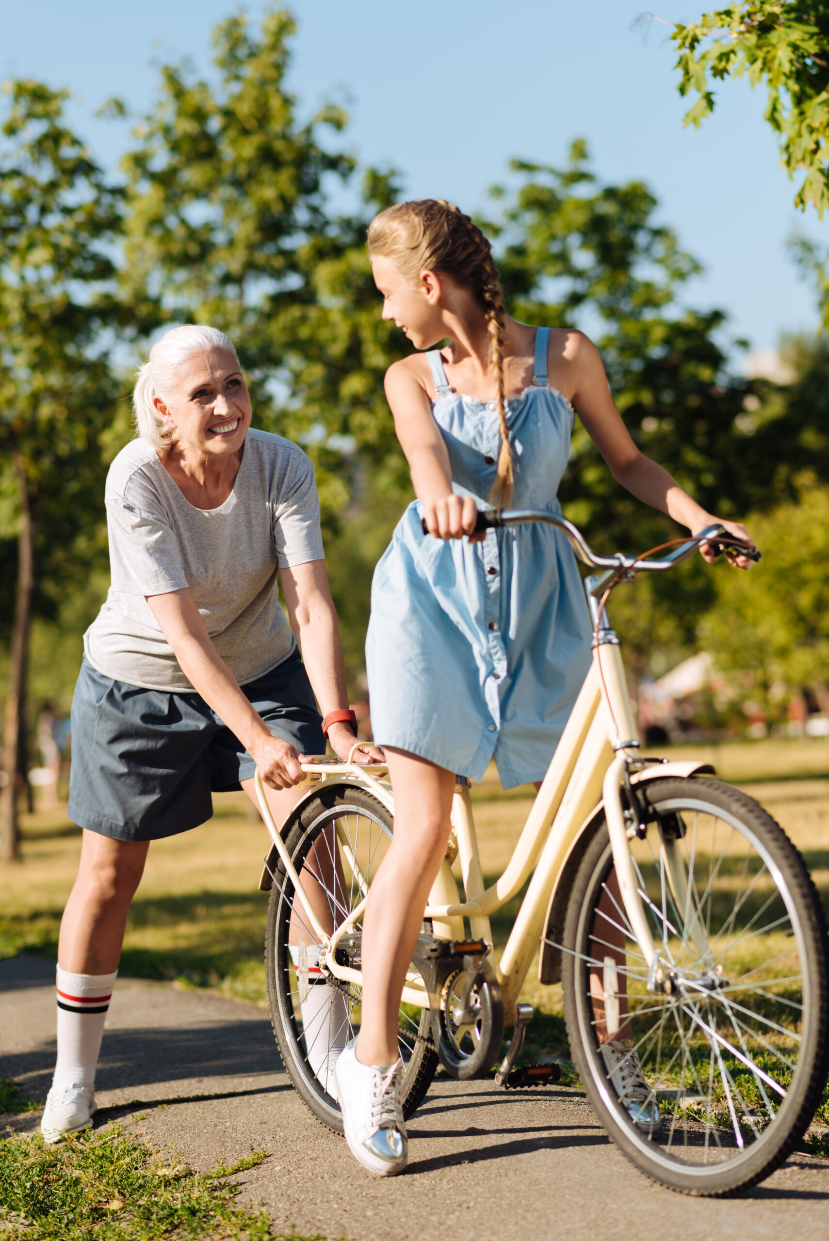 Two individuals, the older figure is holding the back of the bike in support of the younger figure who is smiling and looking back at them.